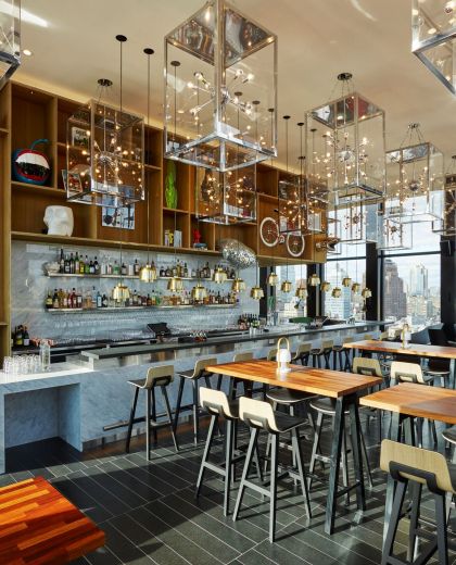Binnen in cloudM New York Bowery rooftop bar met hoge houten tafels, een wit marmeren bar en moderne verlichting