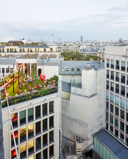 View of a hotel rooftop bar with green grass and red furniture, overlooking Paris